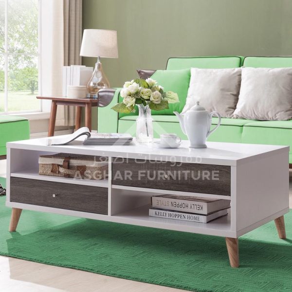 A mid-century modern coffee table with a white body, a dark wooden drawer, and an open shelf. It is supported by four tapered wooden legs.