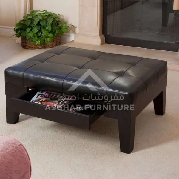 A large square black tufted leather ottoman with a pull-out drawer.