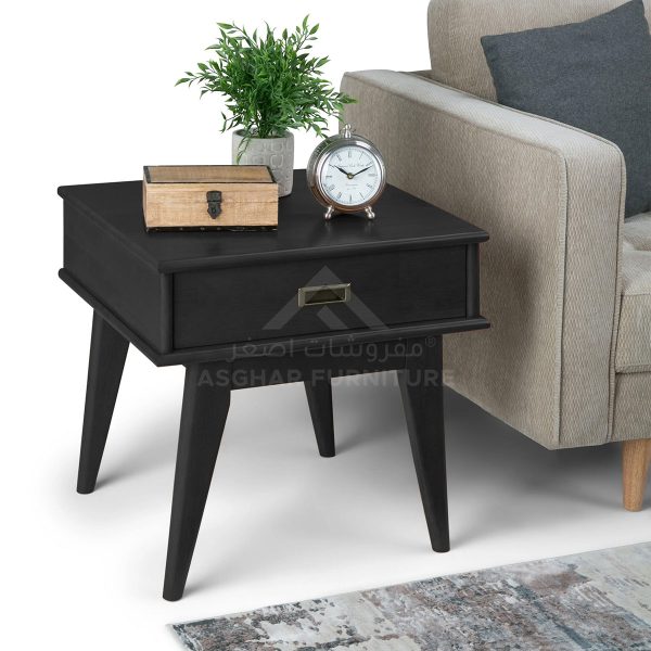 A sleek black side table with one drawer, splayed legs, and topped with a plant, an alarm clock, and a wooden box.