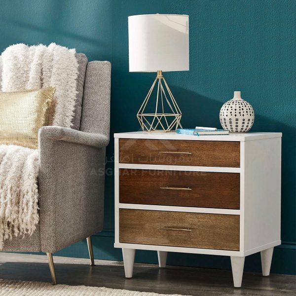 A white three-drawer nightstand with drawers in varying wood tones next to a gray armchair.