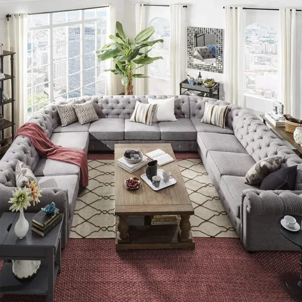 A huge gray U-shaped sectional sofa with deep button tufting and a classic wood coffee table.