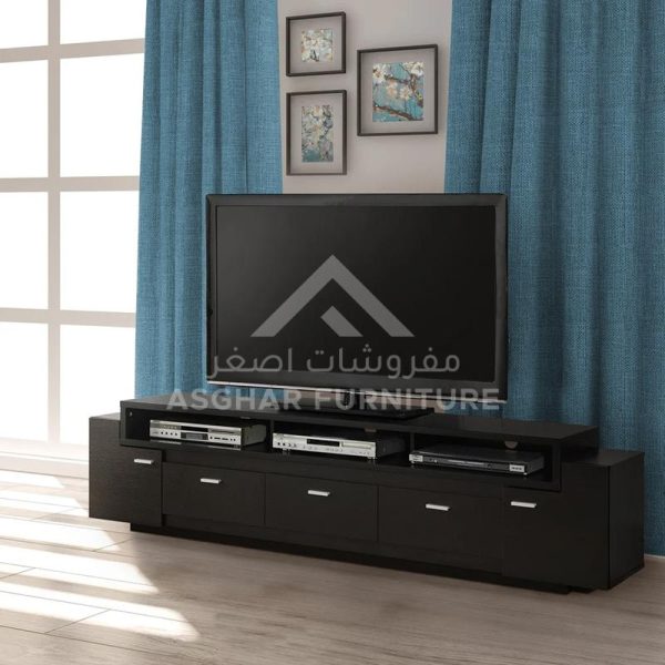 A black TV unit with a television, three drawers, and two shelves, in a room with blue curtains.