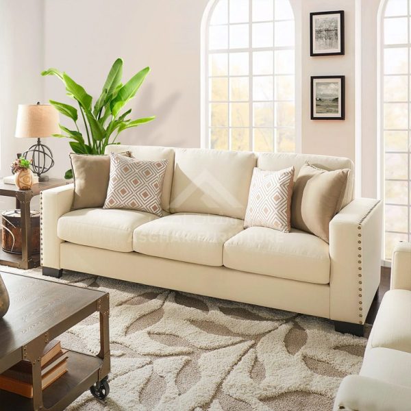 A beige fabric sofa with decorative studs and pillows, with a wooden coffee table and a leafy rug.