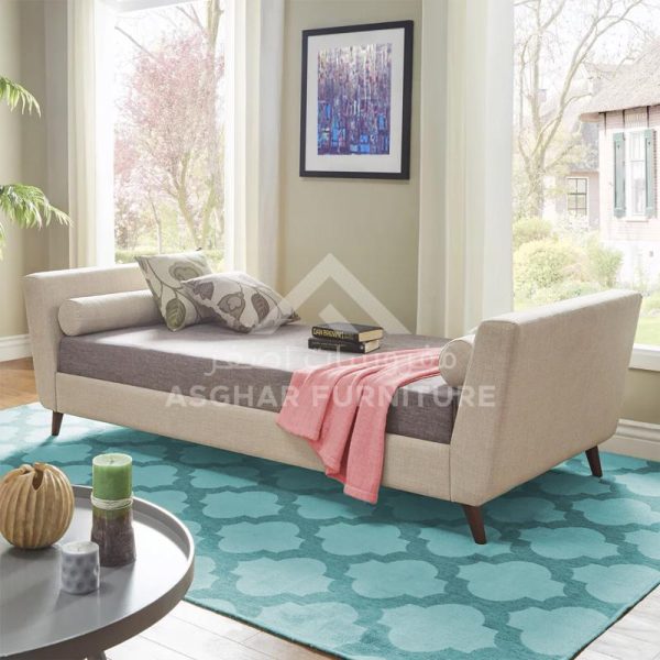 A modern beige daybed with a bolster cushion and a pink blanket, on a turquoise patterned rug.