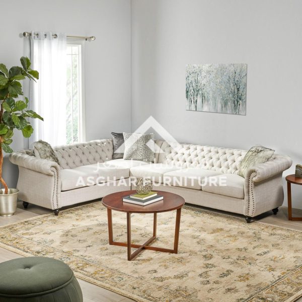 A beige chesterfield sectional sofa with tufted back and roll arms, and a round wooden coffee table.