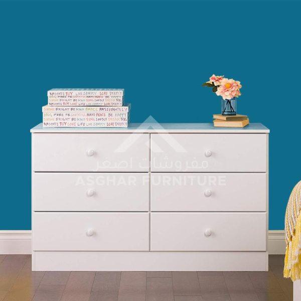 A classic white six-drawer dresser with round knobs, adorned with books and a vase of flowers.