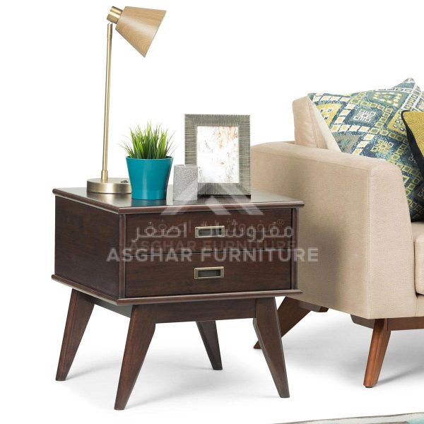 A retro dark wood end table with a single drawer, splayed legs, and a bronze lamp with a plant and framed picture on top.