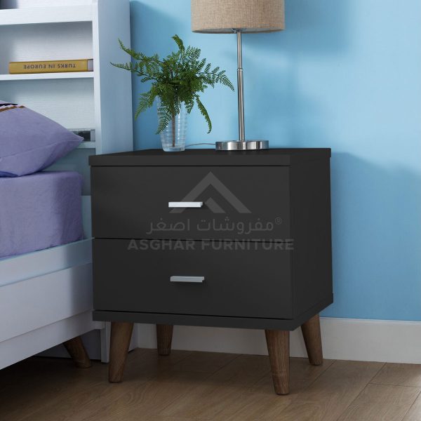 A contemporary black nightstand with two drawers, splayed wooden legs, and a silver lamp with a plant.
