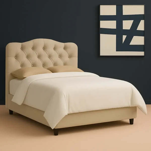 A cream tufted upholstered bed with matching bedding, against a dark blue wall with abstract art.