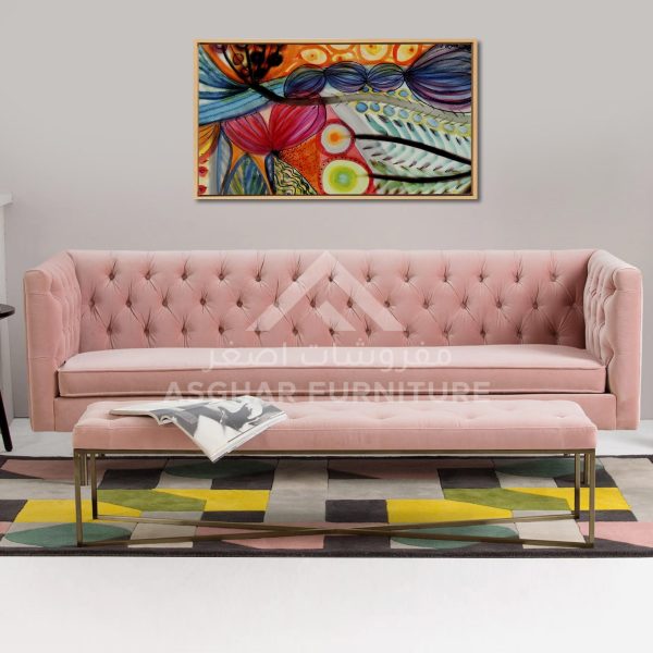 A light pink velvet tufted sofa with a matching tufted ottoman and a colorful abstract rug and art.