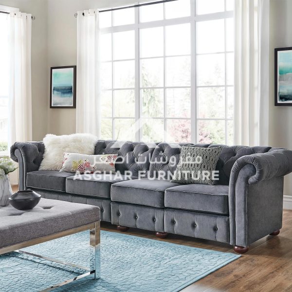A dark gray chesterfield sofa with a tufted back and pillows, and a matching tufted ottoman in a modern living room.