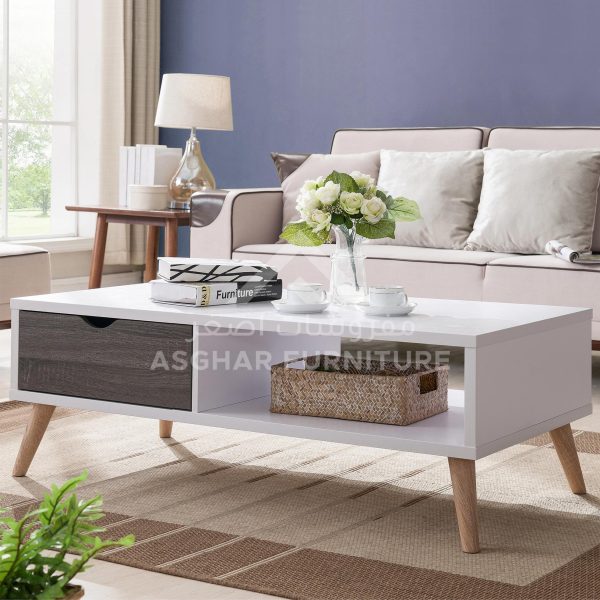 A white rectangular coffee table with a dark wood drawer, an open shelf, and splayed wooden legs.