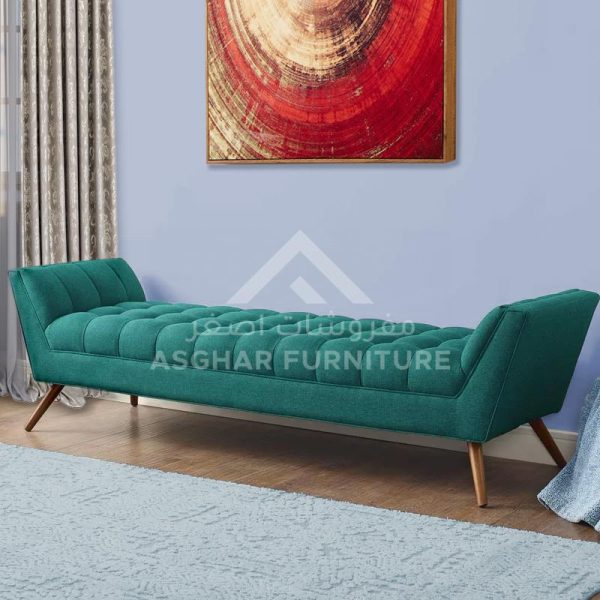 A modern, tufted turquoise bench with flared arms and light wood legs, placed on a light blue rug.