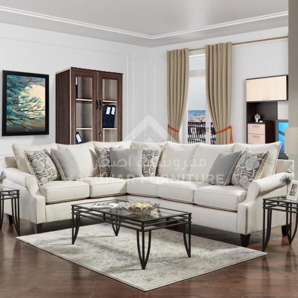 A beige sectional sofa with various pillows, a glass coffee table, and a wooden cabinet in a traditional living room.
