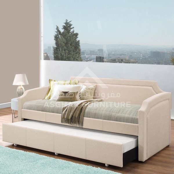 A large cream-colored daybed with a trundle bed underneath, and a collection of cushions and a throw.