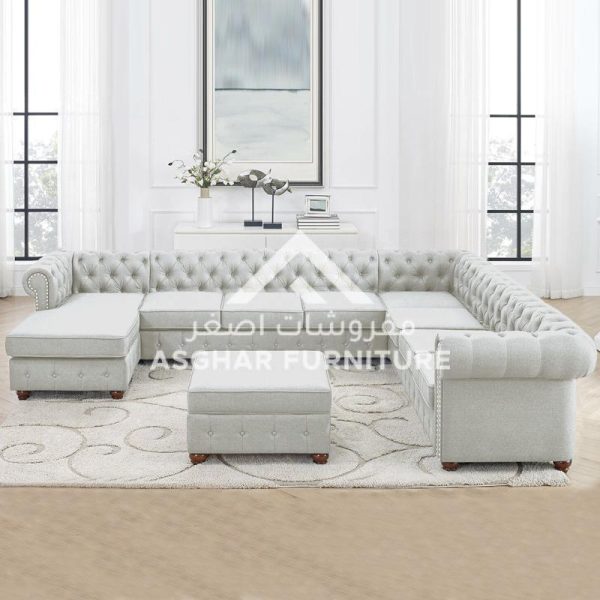A white chesterfield U-shaped sectional sofa with a tufted back and roll arms, a chaise lounge, and a storage ottoman.
