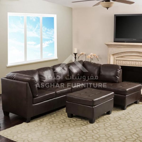 A traditional living room with a brown leather sectional sofa, a tufted ottoman, and a fireplace with a TV on top.