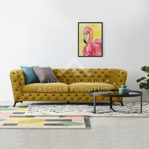 A large yellow tufted chesterfield sofa with pillows, a black coffee table, and colorful abstract art.