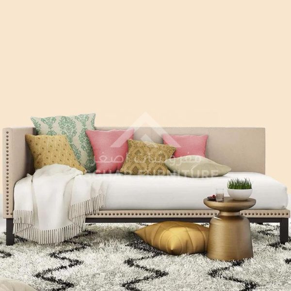 A beige daybed with nailhead trim, a mix of colorful cushions, and a fringed blanket on a patterned shaggy rug.