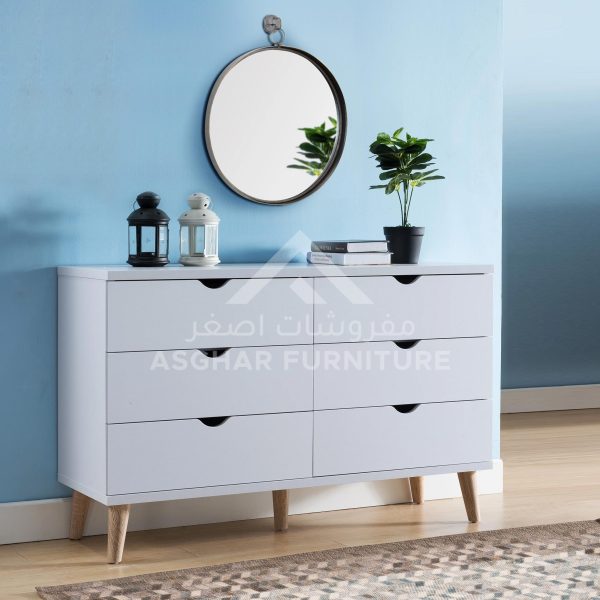 A stylish white six-drawer dresser with unique cutout handles and splayed wooden legs, below a round mirror.