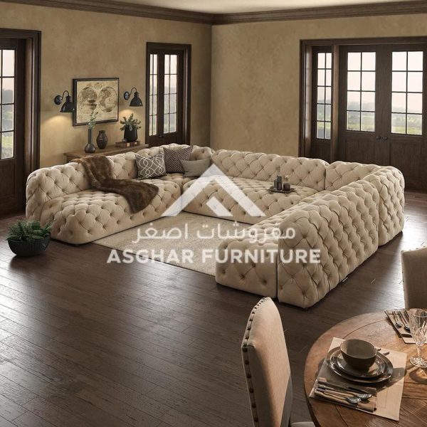 A spacious beige chesterfield sectional sofa with tufted upholstery, and a throw blanket, on a beige rug.