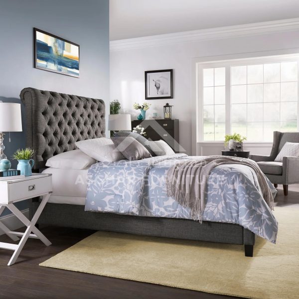 A dark gray upholstered tufted bed, a white x-shaped nightstand, and a light yellow rug.