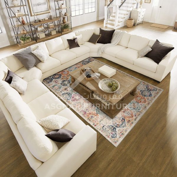 A gray fabric U-shaped sectional sofa with various pillows, a wooden coffee table, and a colorful patterned rug.