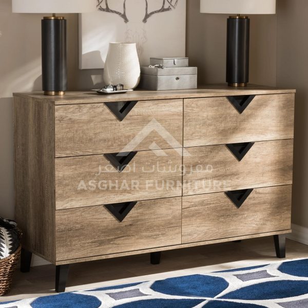 A rustic light wood six-drawer dresser with black triangular cut-out handles, adorned with lamps and decor.