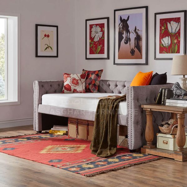 A stylish grey upholstered daybed with a tufted back and sides, nailhead trim, and storage baskets underneath.