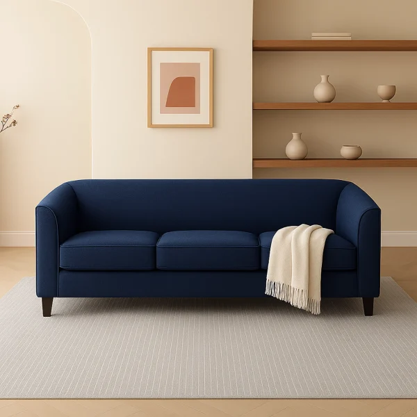 A deep blue three-seater sofa with a cream blanket draped over the armrest, set in a minimalist room.