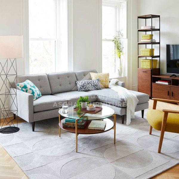 A light gray sectional sofa with a chaise lounge, a round glass coffee table, and a yellow armchair.