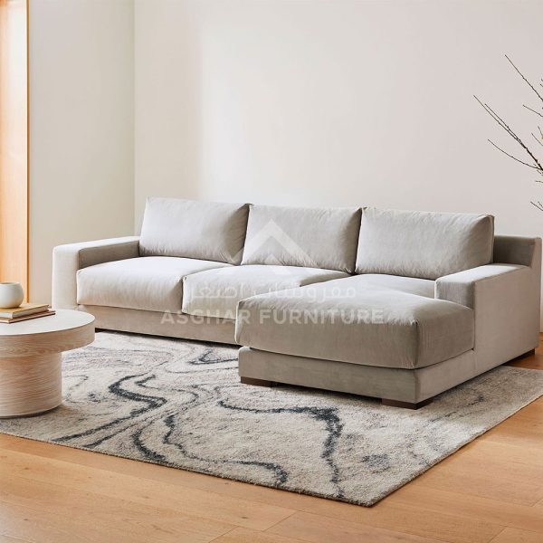A beige fabric sectional sofa with a chaise lounge, and a round white coffee table on a swirly patterned rug.