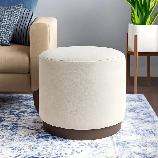 A modern round cream ottoman with a dark brown base on a blue and white patterned rug.