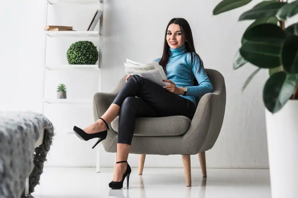 A woman seated in a chair, engrossed in reading a newspaper, with a calm expression on her face.