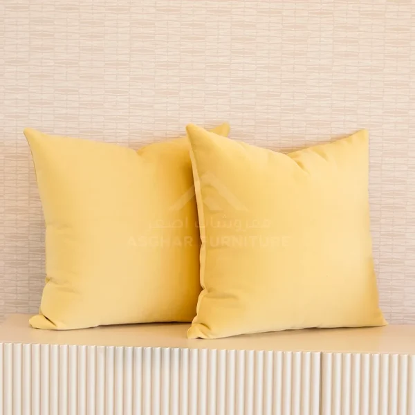 Two square pale yellow cushions on a ridged console table.
