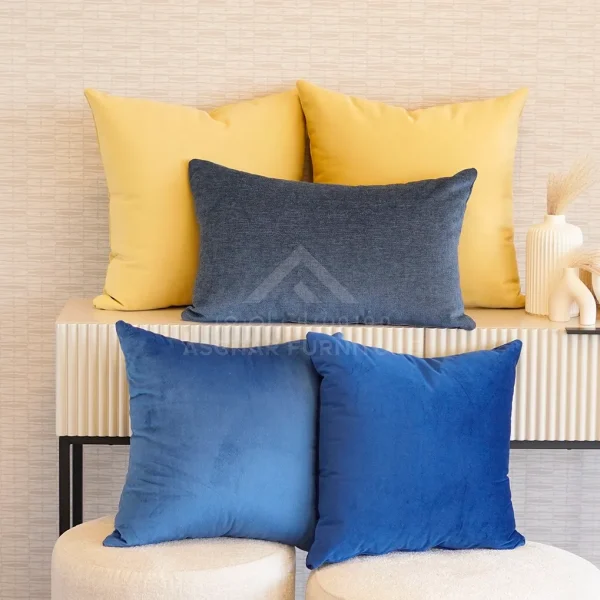 A stack of assorted cushions, including two large yellow ones, a rectangular navy blue one, and two square blue ones.