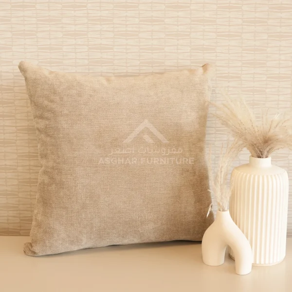 A large, square beige linen-like cushion next to two modern white vases with dried grasses.