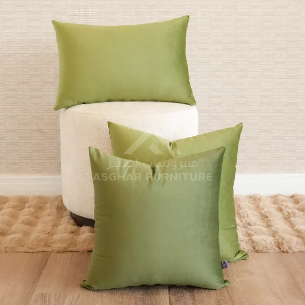 A group of three green velvet cushions in different sizes, arranged with a small white ottoman.