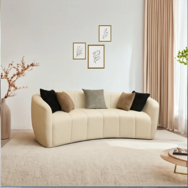 A modern, curved cream sofa with accent pillows, on a light rug, under framed botanical art.