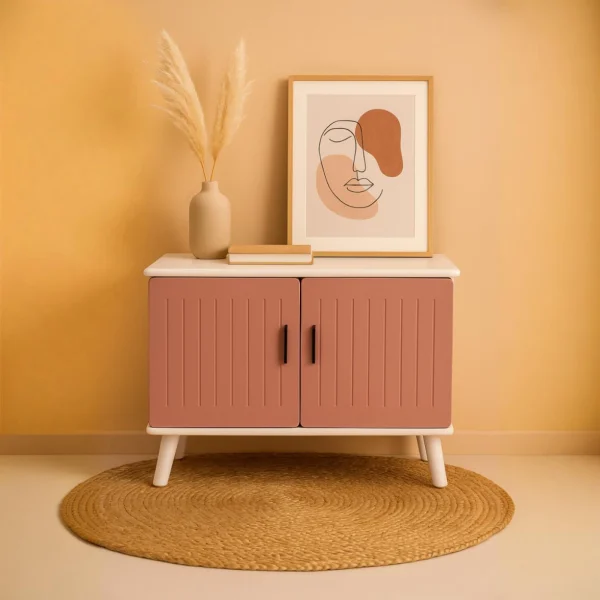 A stylish pink cabinet with slatted doors, a vase of pampas grass, and framed abstract art on top.
