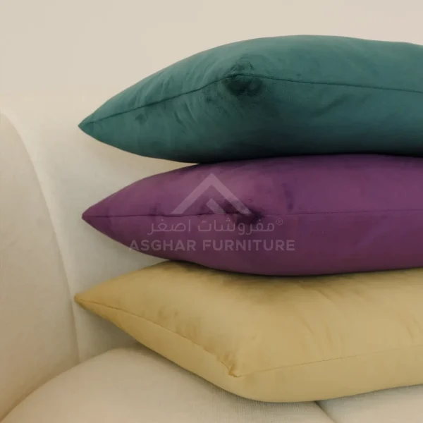 A close-up of three stacked velvet cushions in dark teal, purple, and gold.