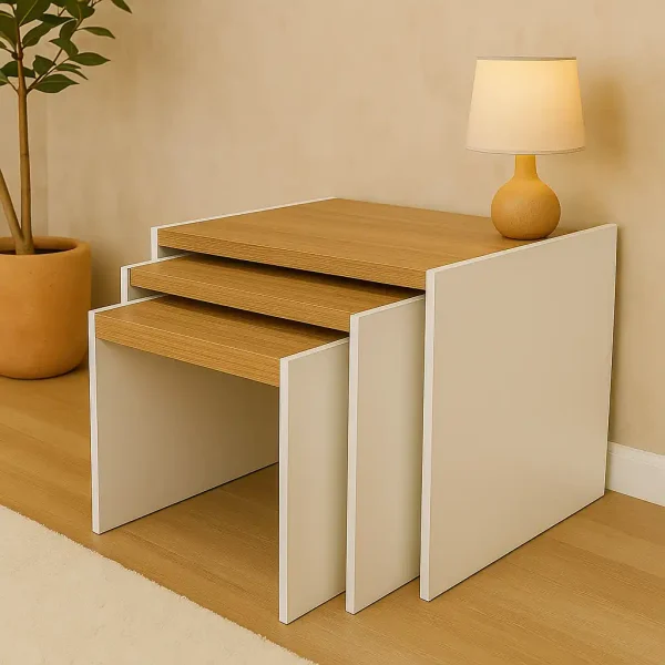 A modern set of nesting tables with natural wood tops and a white frame, with a decorative lamp.