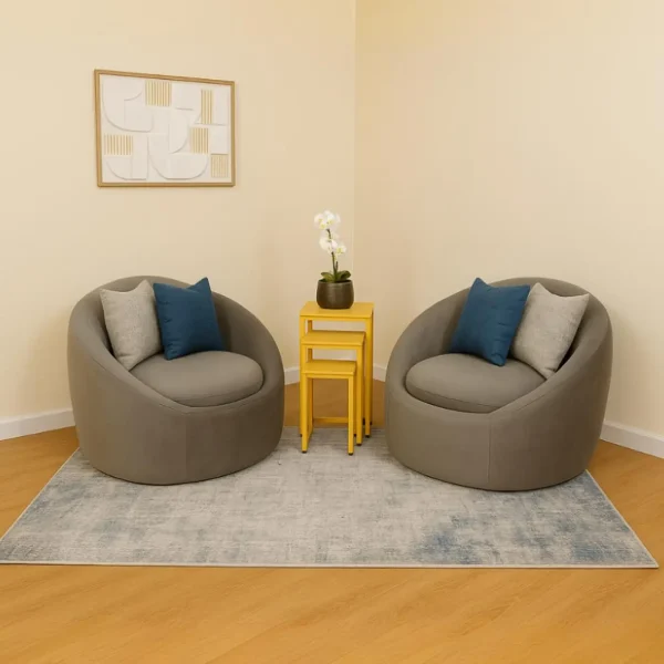 A pair of contemporary, round, gray swivel barrel chairs with blue and light gray throw pillows, positioned on a light gray and blue area rug, flanking a nest of yellow side tables.