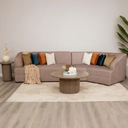 A pink two-piece modular sofa with various colored pillows, and a large round coffee table on a rug.
