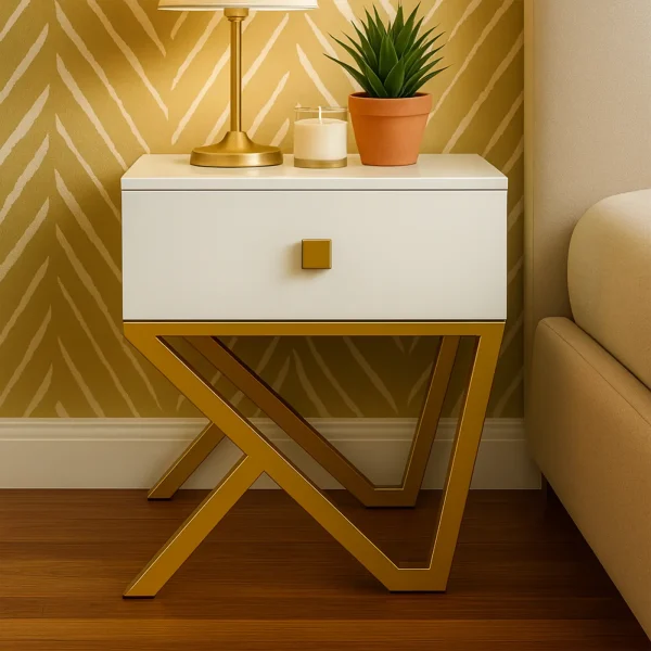 A stylish white nightstand with a gold drawer pull and an abstract, gold metal frame, with a plant and candle.