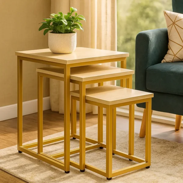 A three-piece set of nesting tables with gold metal frames and light wood tops next to a green armchair.