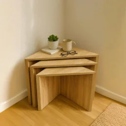 A three-piece set of natural wood, triangular nesting tables with a succulent, mug and glasses.