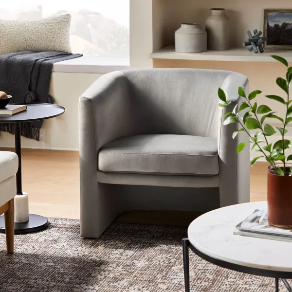A modern living room scene with a light gray velvet club chair, a window seat and various decor.