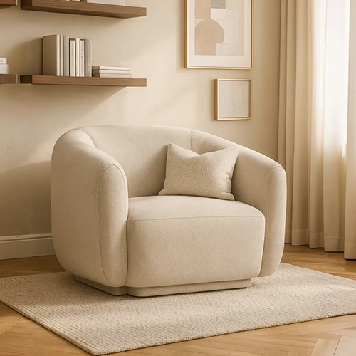 A soft, beige upholstered club chair with a round shape and a pillow in a cozy corner of a room.